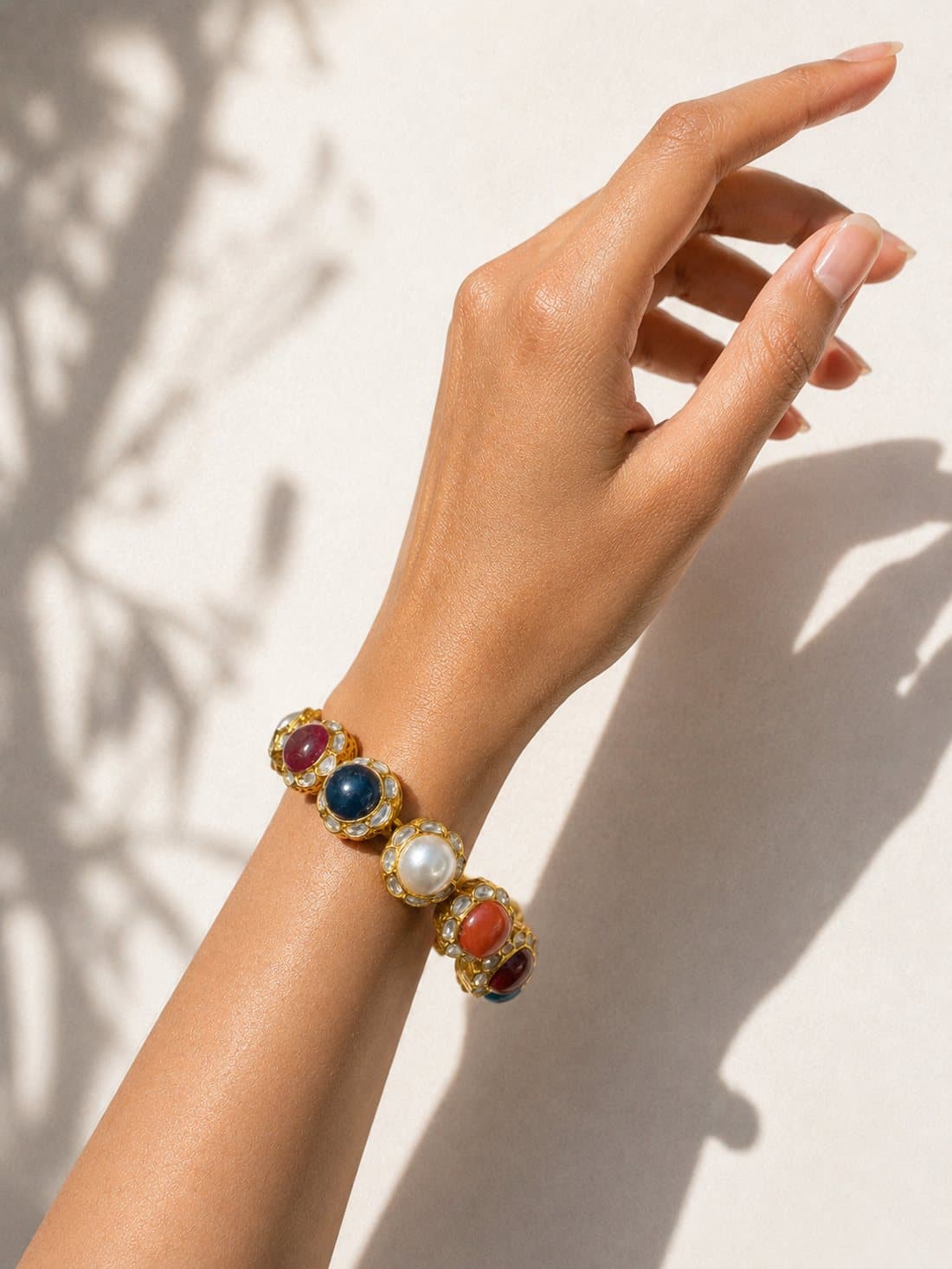 A gold navratna ponchi on the wrist: ruby, sapphire, pearl, coral and the other navratna stones, each set in kundan